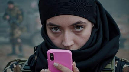 Female military personnel checking smartphone during military operation, demonstrating technological connectivity and personal resilience in challenging combat environment - Powered by Adobe