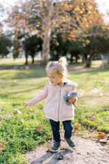 Little girl with a plush cat in her hand walks through the autumn park looking at the fallen leaves