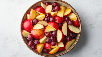A bird is eye view of a bowl of sliced apples, pears, and grapes mixed with honey and yogurt, on a white background