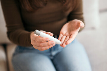 Young woman checking blood sugar level with glucometer at home, monitoring diabetes health on the...