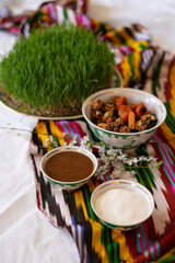A spread featuring a green plate with growing wheatgrass, resting on colorful striped fabric. A bowls with traditional sweets highlighting the richness of the table.