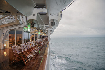 Views onto wet outdoor teak balcony terrace veranda promenade boat deck of ocean liner cruiseship cruise ship with chairs and loungers at sea during 