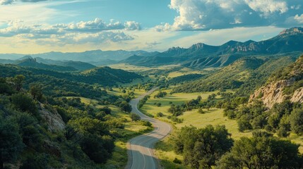 A high-angle view of a winding road cutting through a green valley with distant mountains.