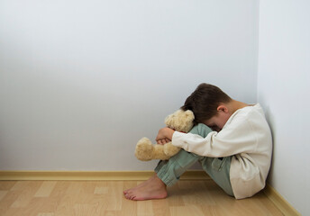 Boy crying with his head down and sitting sad scared on the floor in the corner and hugs his knees. Concept domestic violence and child abuse.