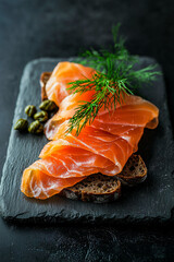 classic Norwegian r&oslash;kelaks smoked salmon with dill, capers, rye bread slices, slate serving board