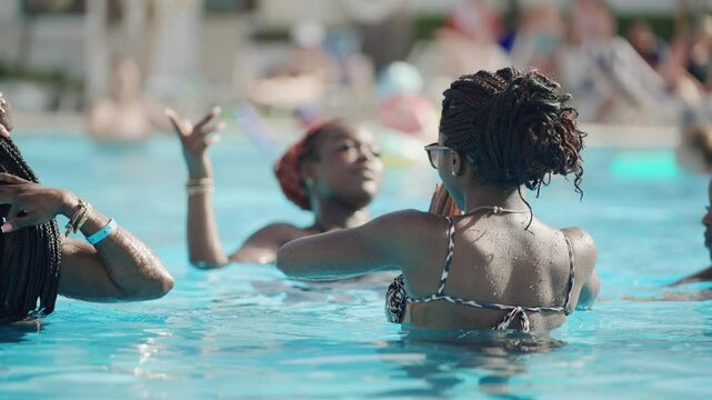 Black african friends having fun in a swimming pool under summer sun, a joyful moment as they splash and interact in slow motion
