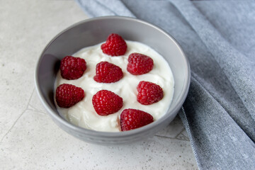 Gray bowl and natural yogurt with berries on the stone marble table.