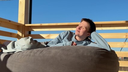 young woman relaxing on shapeless pouf on veranda in sun in warm weather, rest, fresh air