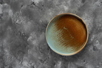Round plate with a rim in a warm colors on a gray concrete background. Minimalistic composition...