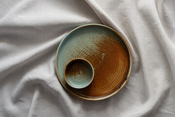 Round plate with a rim in a warm colors on a beige cotton tablecloth. Minimalistic composition with...