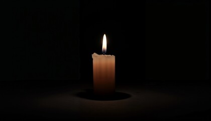 Single burning candle illuminating darkness with soft glow against a black background
