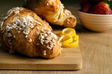 A plate of croissants with powdered sugar and a lemon slice on top. The croissants are sitting on a wooden cutting board