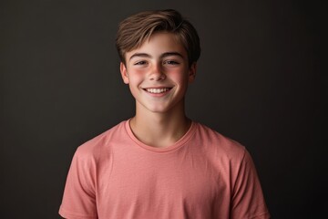 Fototapeta premium Smiling teenage boy in pink t-shirt standing against dark background in studio portrait 