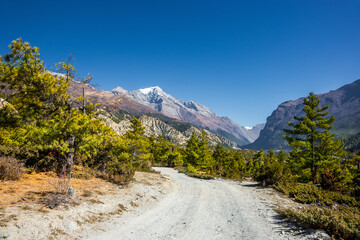 Annapurna circuit trekking route. A new wide gravel road from Humde to Manang and Pisang peak on the horizon. Autumn landscape in Himalaya mountains, Nepal.