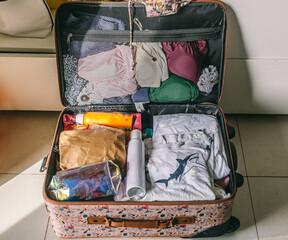 A suitcase is open and filled with clothes. A bottle of sunscreen is on the floor next to the suitcase