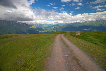 Scenic mountain landscape in Georgia's Svaneti region with a dirt road winding through green hills. Majestic Caucasus mountains and dramatic clouds create a perfect scene for travel and adventure.