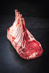 Raw dry aged bone-in back rack of veal loin offered as close-up on a black board