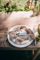 Elegant outdoor wedding place setting with a winged pin on a light brown ruffled linen napkin