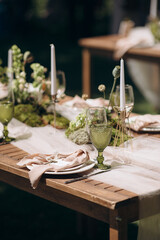 Elegant outdoor table setting with green moss, white flowers, and green-tinted glasses