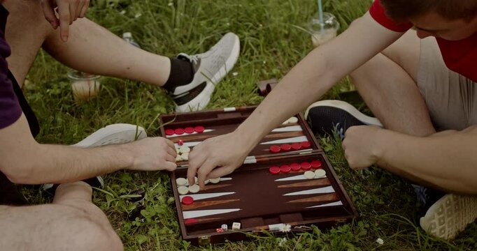Two friends play a game of backgammon in the park on a summer day. They enjoy their time together while playing.