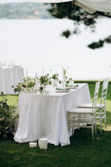 Elegant outdoor wedding presidium with a white tablecloth, white floral arrangements, and ghost chairs