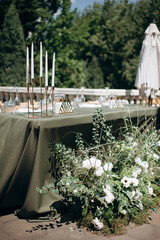 Elegant outdoor wedding presidium with an olive green tablecloth, white plates, and golden candle holders