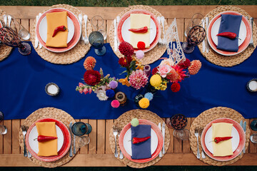 Overhead shot of a vibrant wedding table setting with a blue runner, colorful floral arrangements, and chili pepper accents