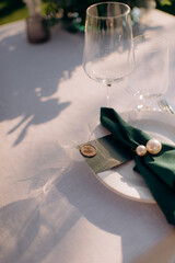 Close-up of an elegant wedding place setting with a white plate, emerald green napkin secured with pearls, and a personalized tag