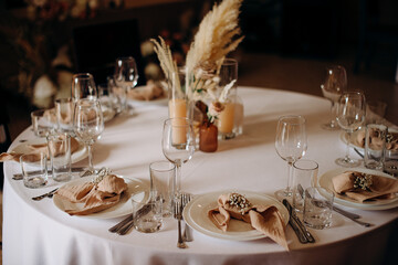 Elegant round wedding table setting with a white tablecloth, beige napkins, simple floral decor, and tall candles