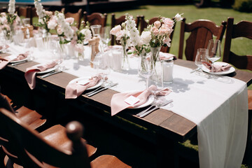 Elegant outdoor wedding table setting with a dark wooden table, white runner, pink napkins, and lush floral centerpieces