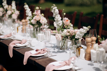 Elegant outdoor wedding table setting with a dark wooden table, white runner, pink napkins, and lush floral centerpieces