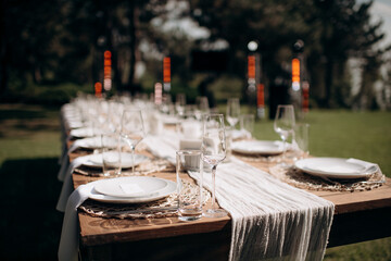 Elegant outdoor wedding table setting with a white tablecloth, tied white napkins, wine glasses,...
