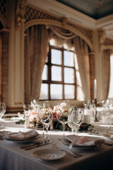 Elegant indoor wedding table setting with a white tablecloth, beige plates, tall wine glasses, and a silver candelabra with white candles