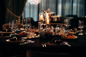 Elegant indoor dinner party table setting with a black tablecloth, gold-rimmed plates, dark...