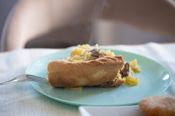 Steaming slice of homemade meat and potato pie on light blue plate with fork