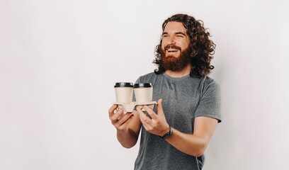 Fototapeta premium A cheerful man joyfully holding two ecofriendly coffee cups, exuding happiness against a clean, vibrant backdrop