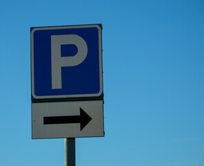 A prominent parking sign indicates available spaces with a directional arrow, set against a vibrant blue sky suggesting a sunny day, likely in an urban area