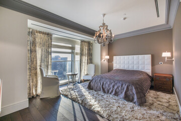 Cozy home bedroom interior with elegant curtains on the window, a beautiful chandelier, carpet and furniture in the sunlight.