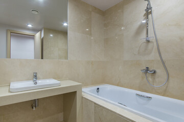 Modern bathroom design decorated with beige tiles. Bath with shower, square mirror over the sink.