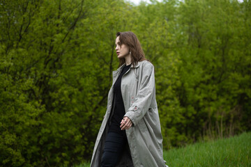 young woman in coat in spring greenery, trees and grass in nature