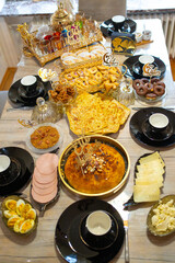 Traditional Eid breakfast table set with festive foods: sweet dessert centerpiece, cheeses, cold cuts, boiled eggs and drinks. A cozy and cultural morning meal celebration