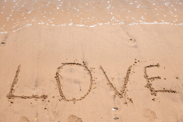 The word “LOVE” etched in sandy beach shore, symbolizing romance, summer vibes, and emotional connection.