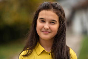 Fototapeta premium Portrait of a happy teenage girl outside, looking at the camera and smiling.