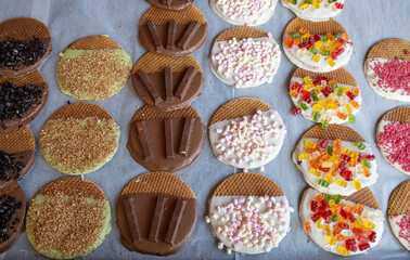 Variety of fresh baked syrop caramel waffles decorated with different toppings, chocolate, cream, fruit and berries, jelly sweets in bakery with confectionery shop, old Volendam, Dutch sweets