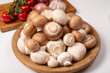 White and brown champignons mushrooms fresh uncooked on wooden plate copy space on white background