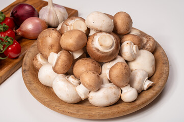 White and brown champignons mushrooms fresh uncooked on wooden plate copy space on white background