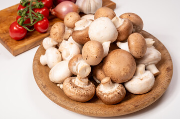 White and brown champignons mushrooms fresh uncooked on wooden plate copy space on white background
