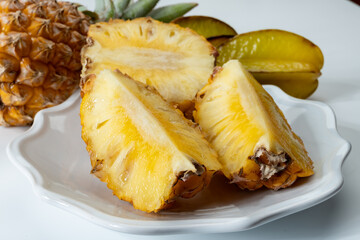Two whole fresh ripe pineapples or sweet baby ananas and starfruits on white background close up