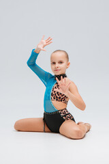 cheerleader in a costume with a blue sleeve and leopard print, adorned with rhinestones, sits on the floor. One arm is raised, and the pose resembles a dance or gymnastics move.