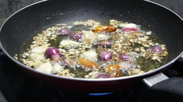 cooking or frying spices consisting of shallots, garlic, turmeric, candlenuts on a teflon pan with hot oil